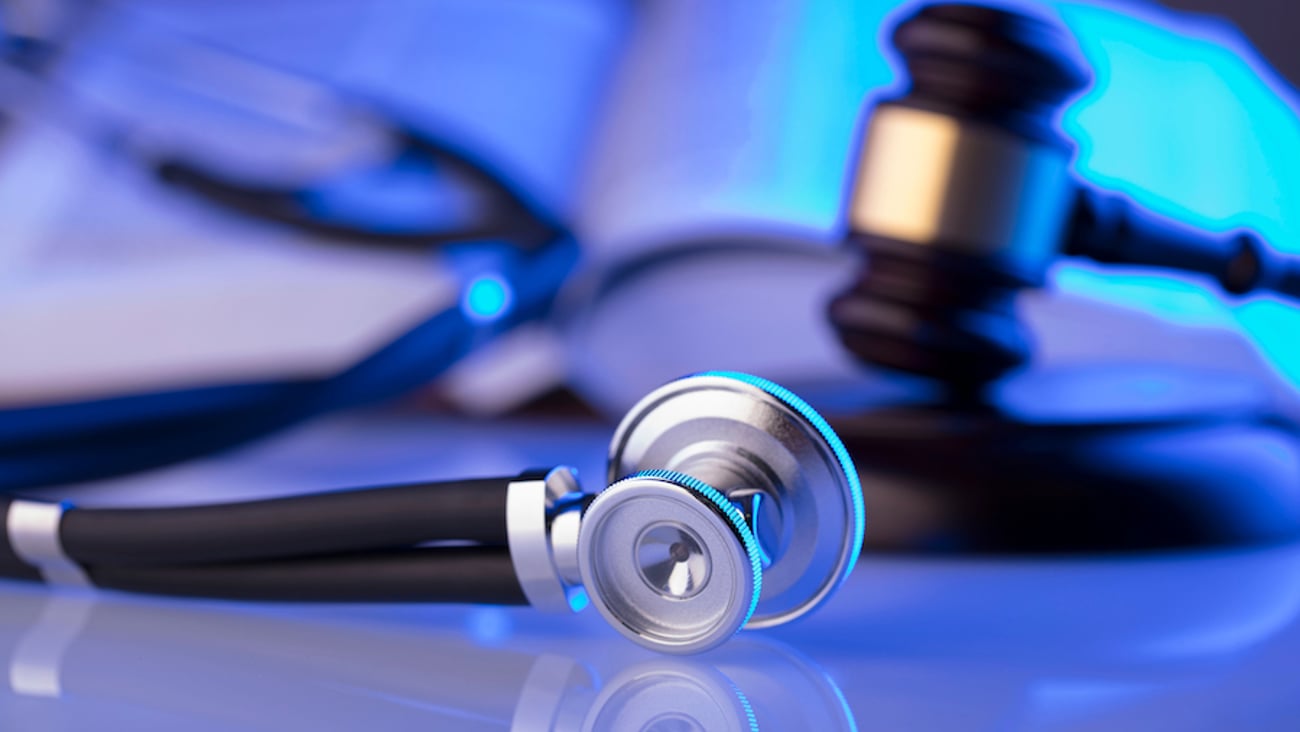 A stethoscope sits on a table with a gavel behind in. 