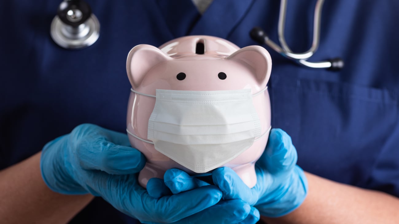 Piggy bank with a surgical mask held by a healthcare worker