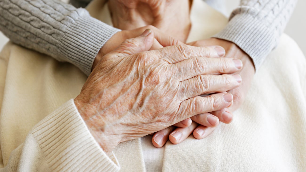 Close of up a young woman gently hugging an elderly relative from behind