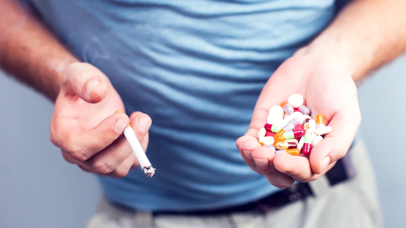 man-holding-pills-and-cigarette