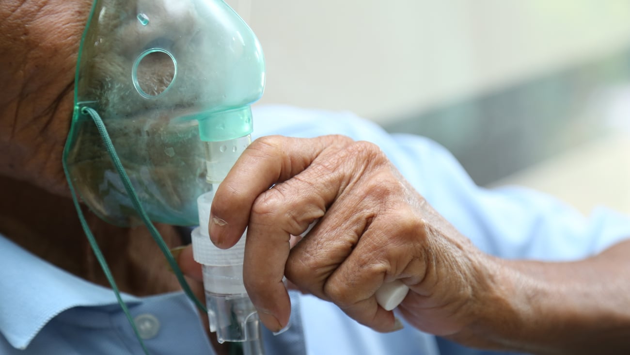 Older man holding breathe apparatus up to his face 