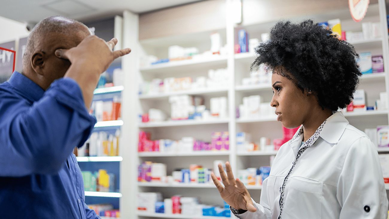 a patient holds his head while describing pain symptoms to a pharmacist