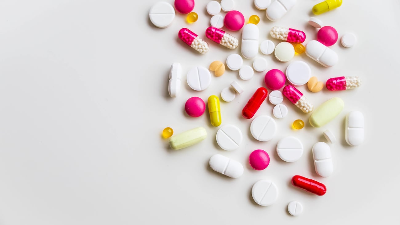 Lots of pink and white pills spread out on a white background