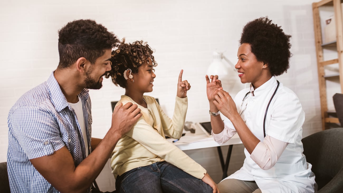 father and child with hearing aid talk to female hcp