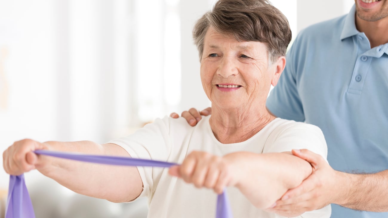 Older woman holding an exercise band out in front of her with both hands