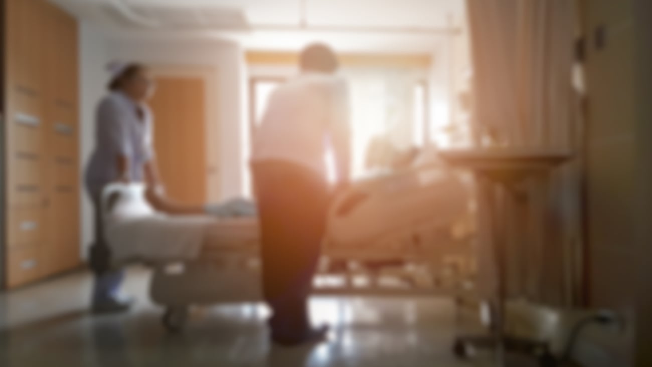 Blurry wides shot of a hospital room with a doctor leaning over a patient