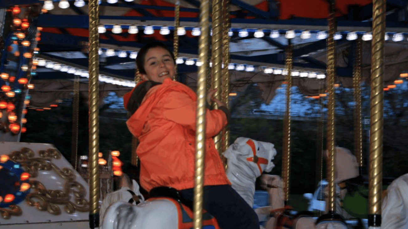 A boy in red jacket, smiling as he rides a merry go round hore