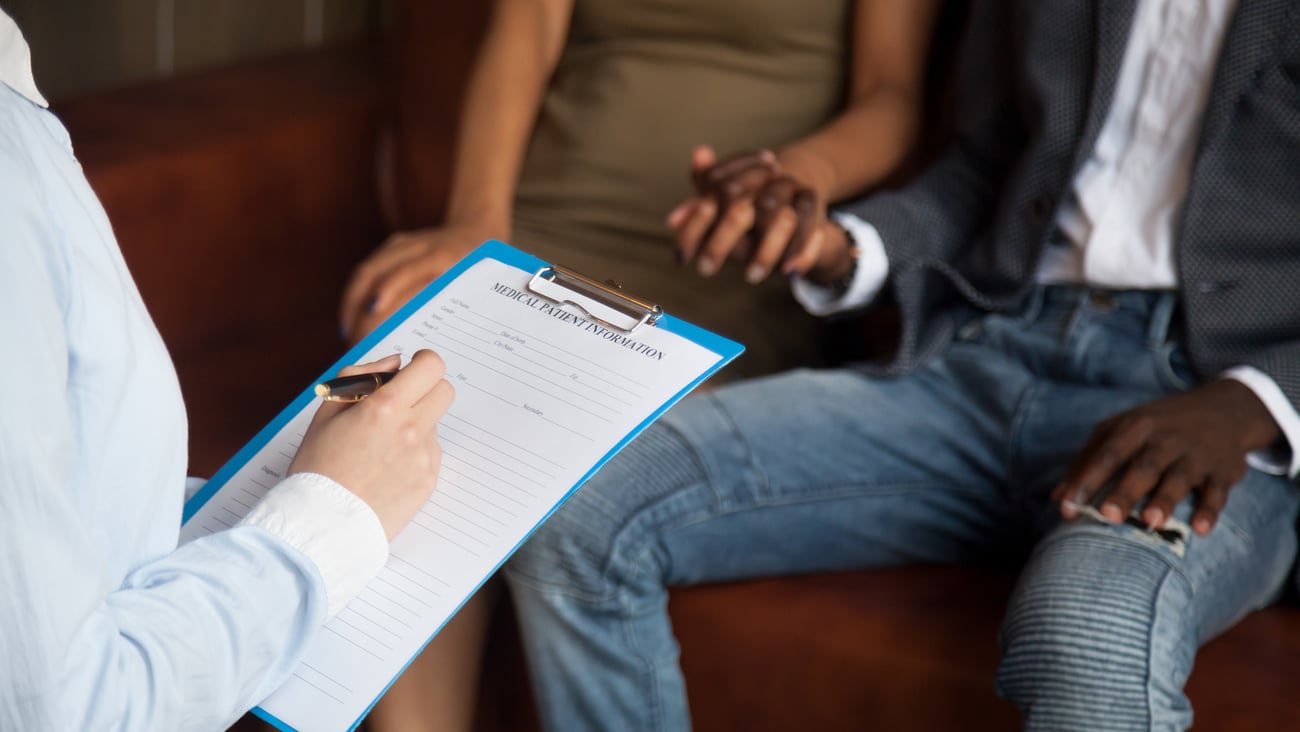 A couple holding hands with a doctor filling out a form in the foreground