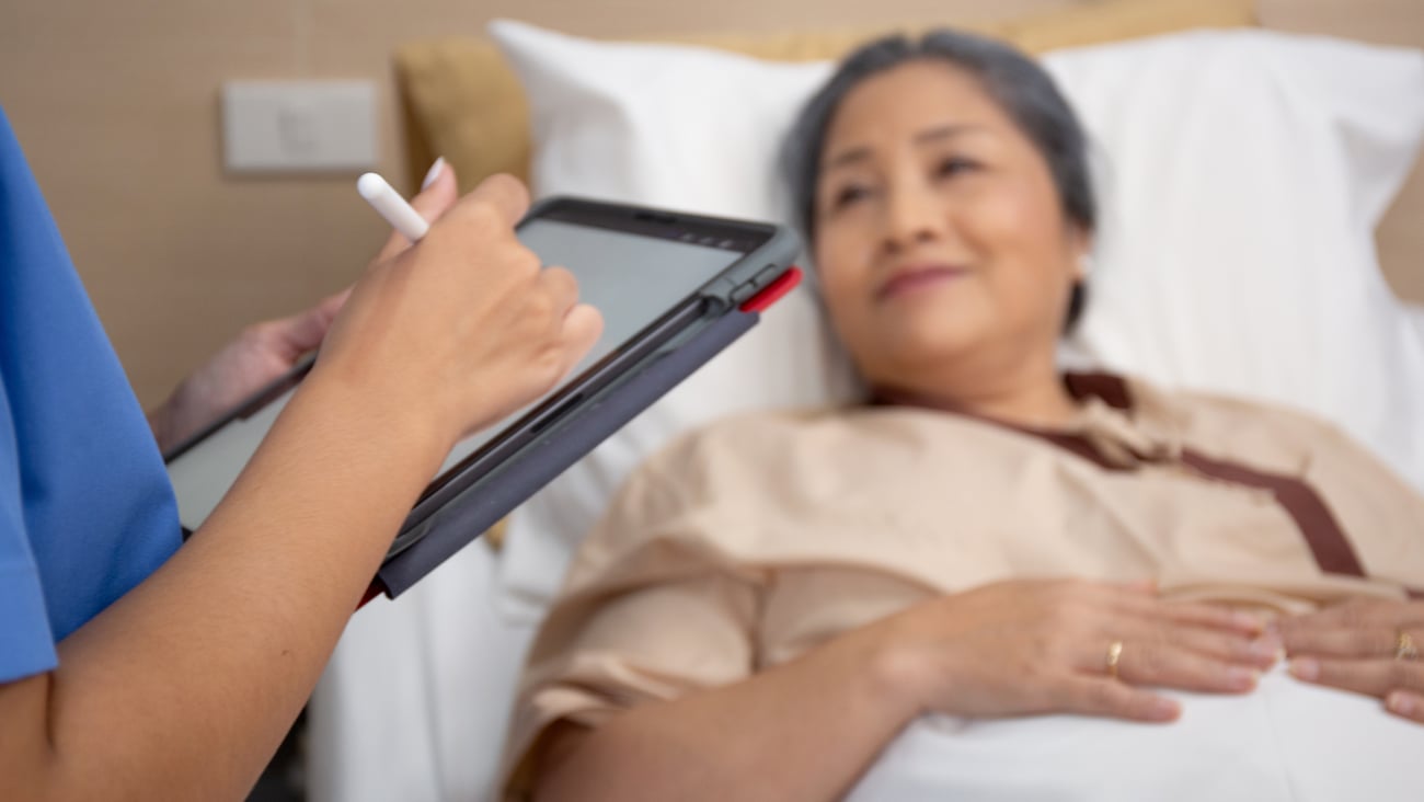 Older Asian woman patient in the background as nurse takes notes