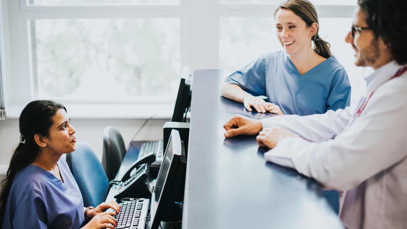 female medical receptionist at desk talking to two female colleagues