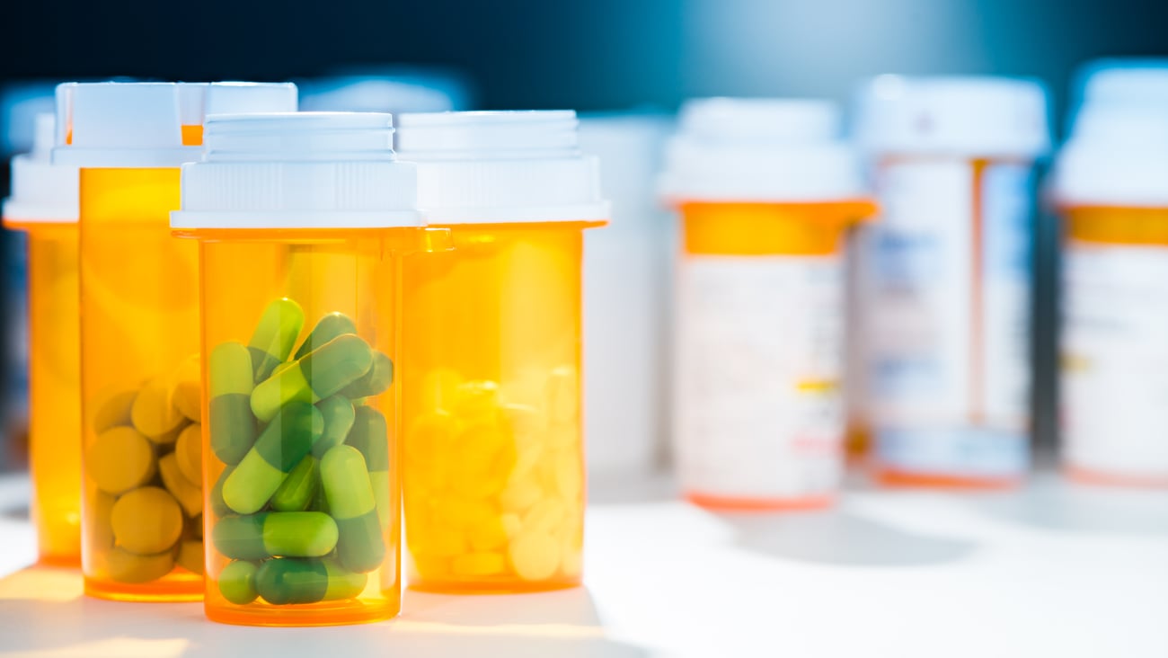 group of prescription pill bottles with various pills in each bottle; bottle in focus has green capsules