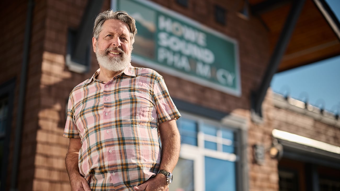 Older whgite man with a beard standing in front of a shop