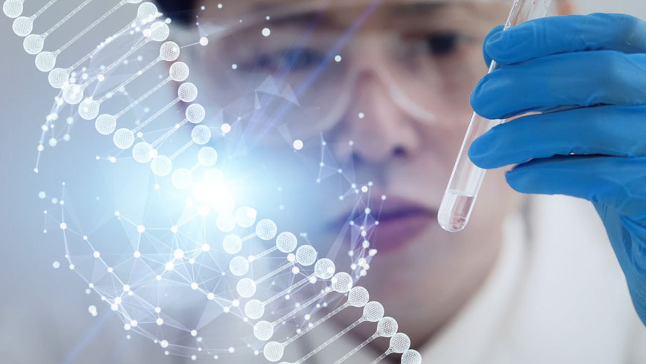 a young Asian male researcher holds a test tube while a DNA strand is superimposed over the image