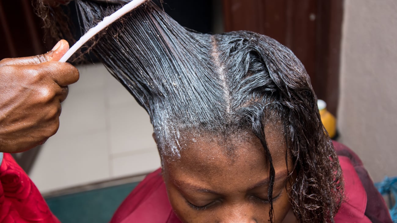 Black woman at salon having relaxer formula combed through hair