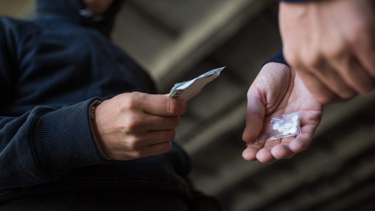 A young man paying another young man for a packet of pills