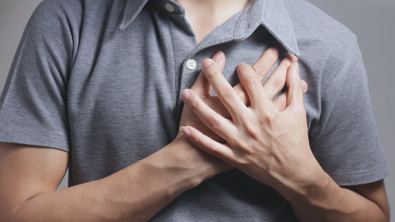 chest of young white man, gray shirt, holding left side of his chest