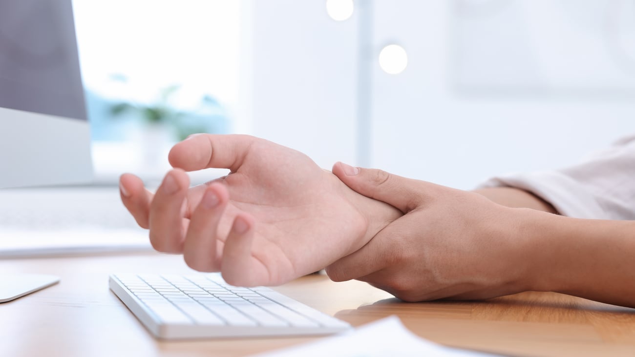 A person suffering from wrist pain at their desk