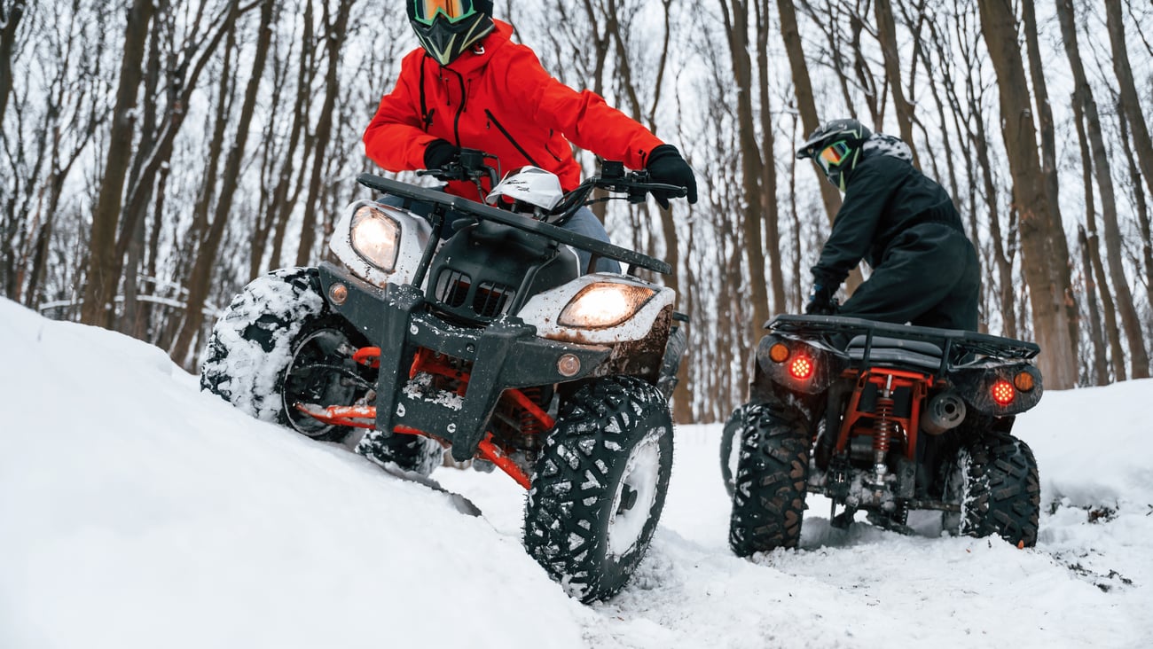 Two young people on ATVs in the snow in the forrest