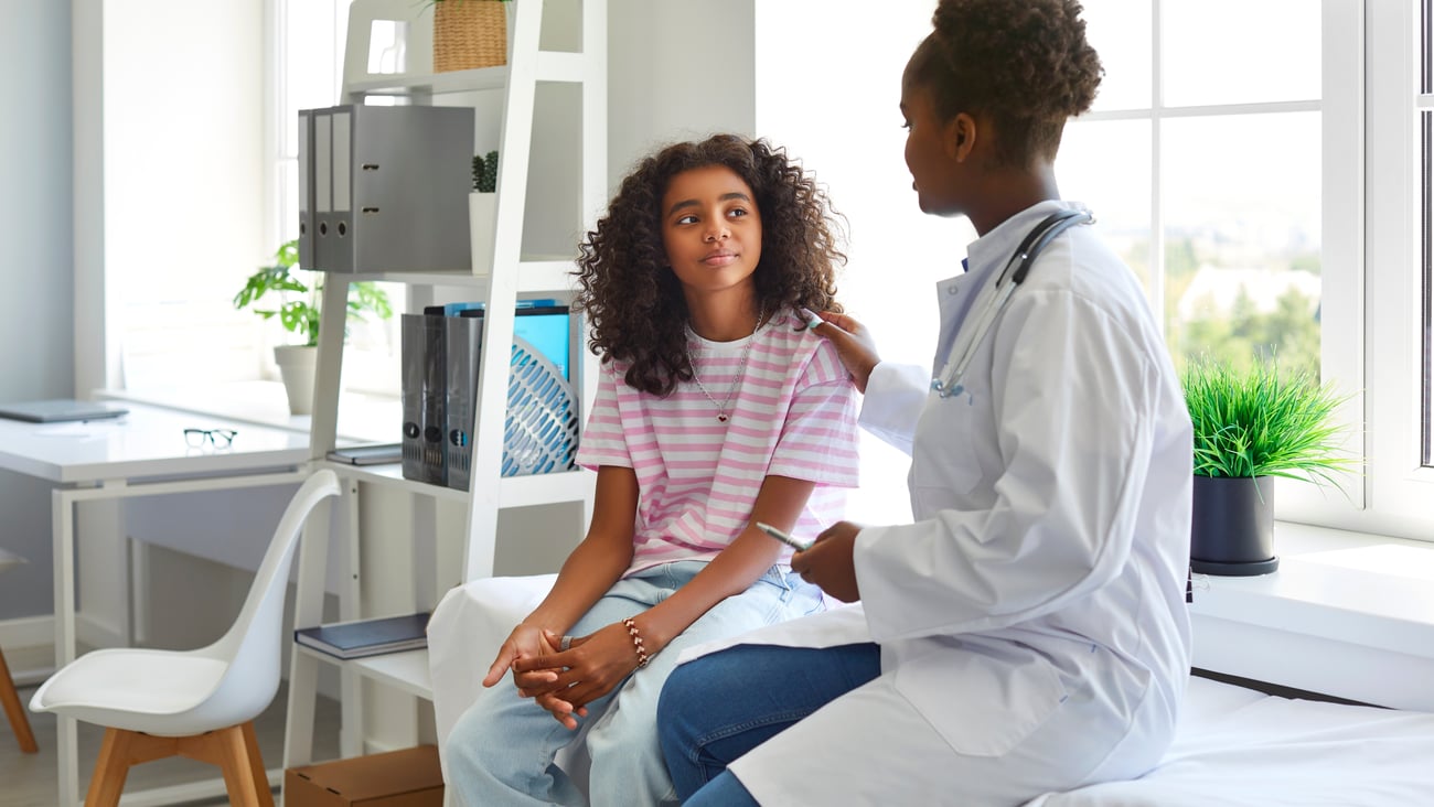 A doctor touches the shoulder of a teenage patient.