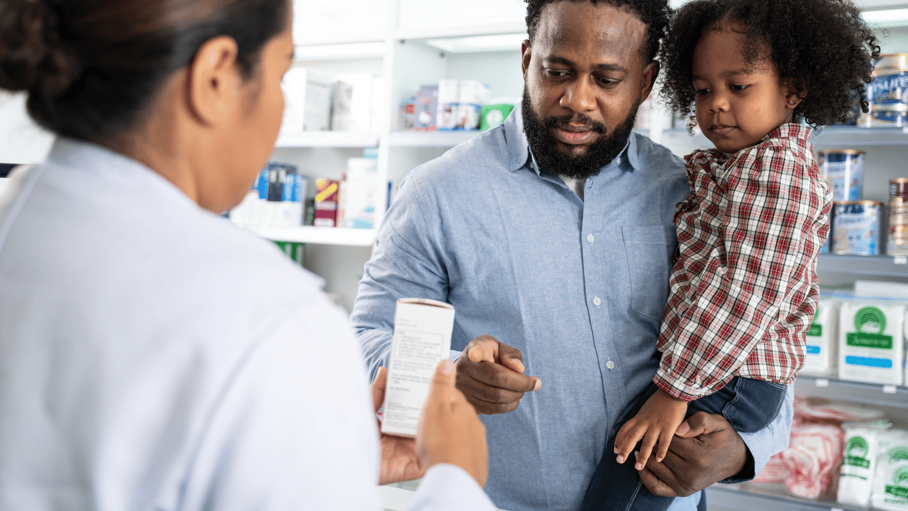Female pharmacist counselling a black man with a young girl in his arms
