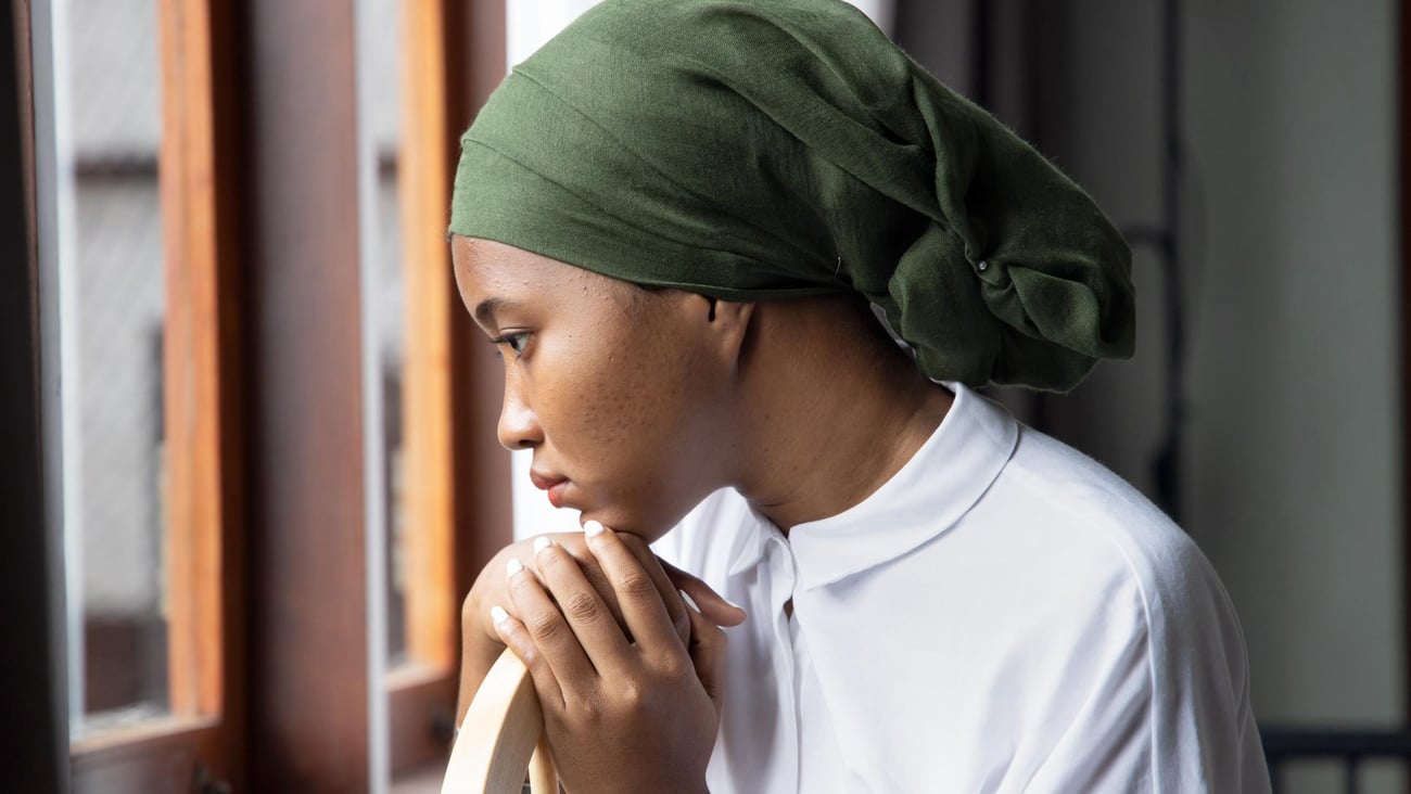 Black woman wearing green scarf on head suggesting hair loss, looking sad