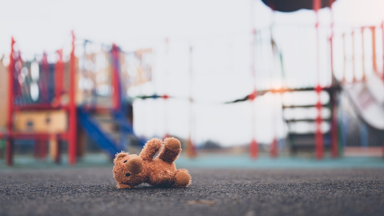 Abandoned teddy bear in the foreground of a picture of playground