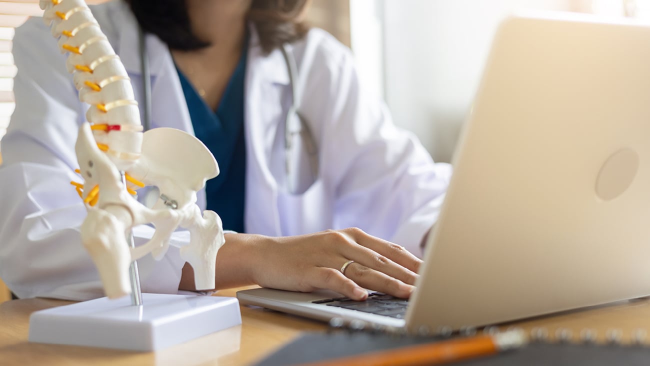 Woman healthcare professional typing on a laptop with a pelvic bone display in the foreground