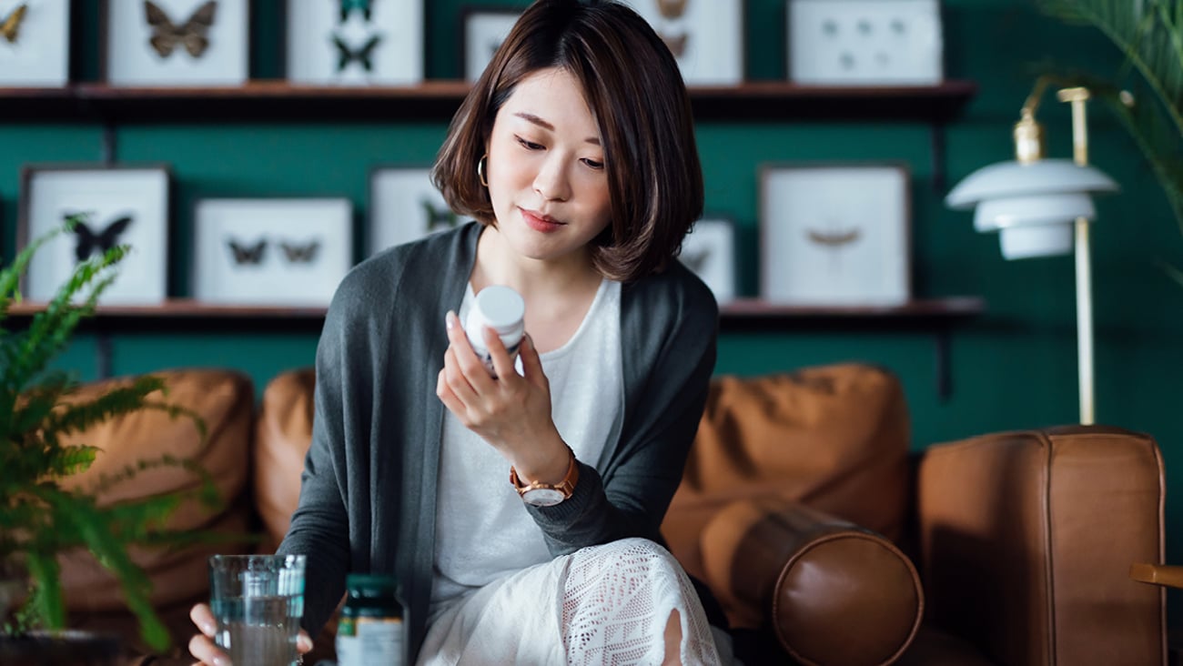 A young Asian woman in a well-decorated room looking contemplatively at the pill bottle