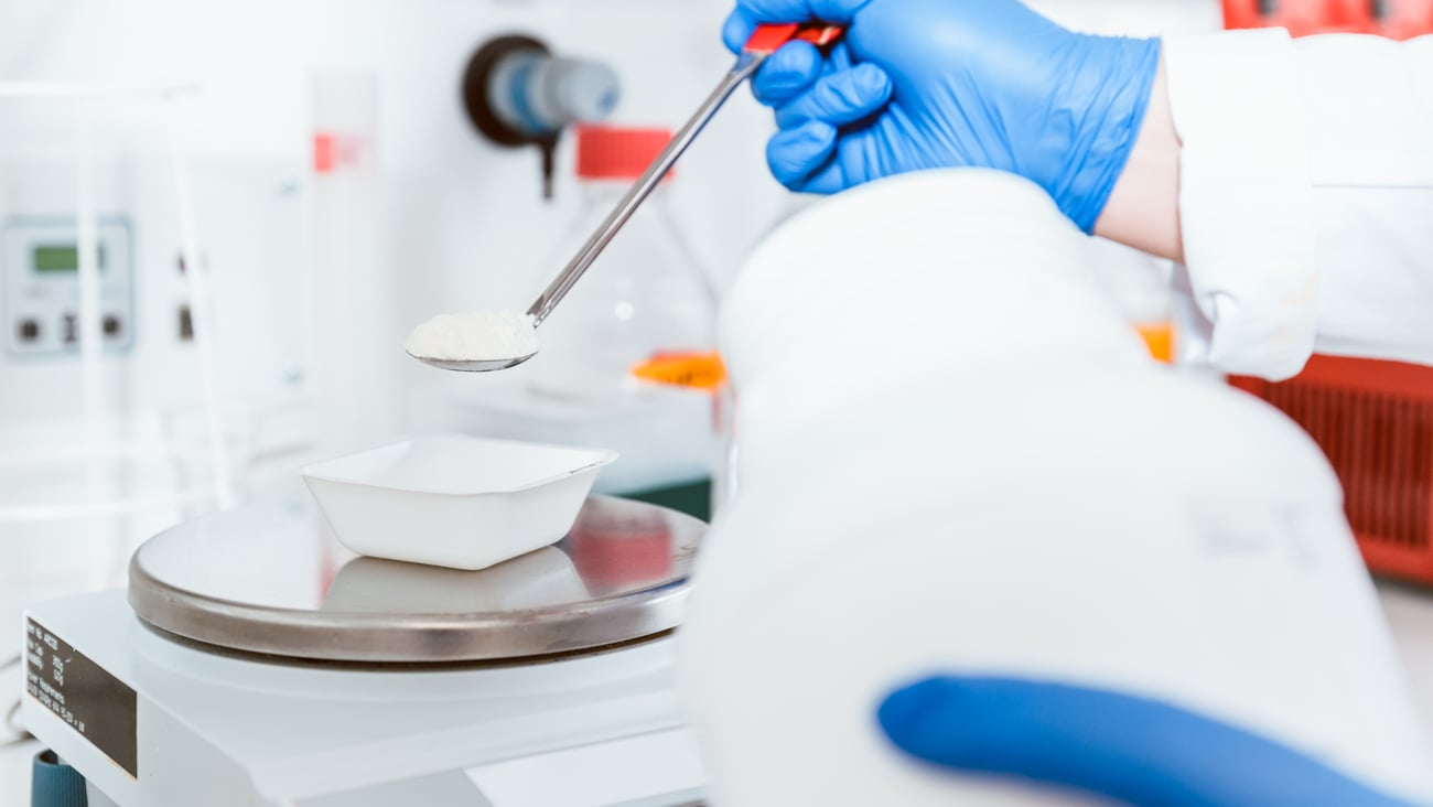 Close up of the blue gloved hands of a pharmacist working with raw ingredients in a compouding pharmacy