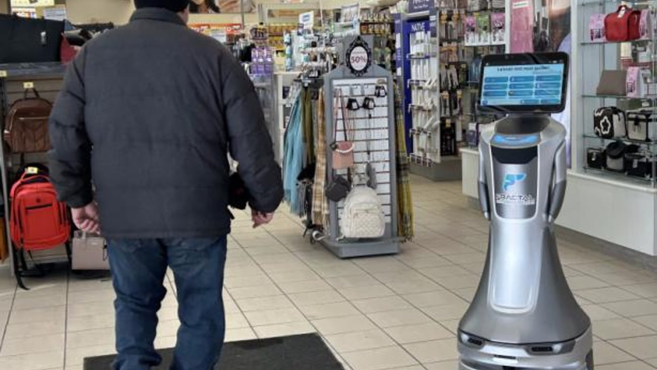 Man in retail store walks toward robot that as a screen for its head.