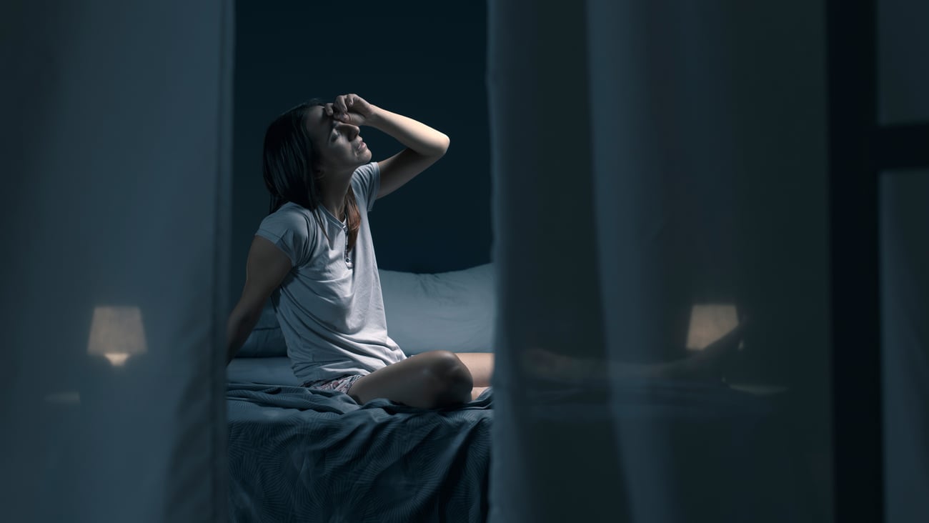 Woman on bed at night, stressed, hand on head, tired or hot, can't sleep
