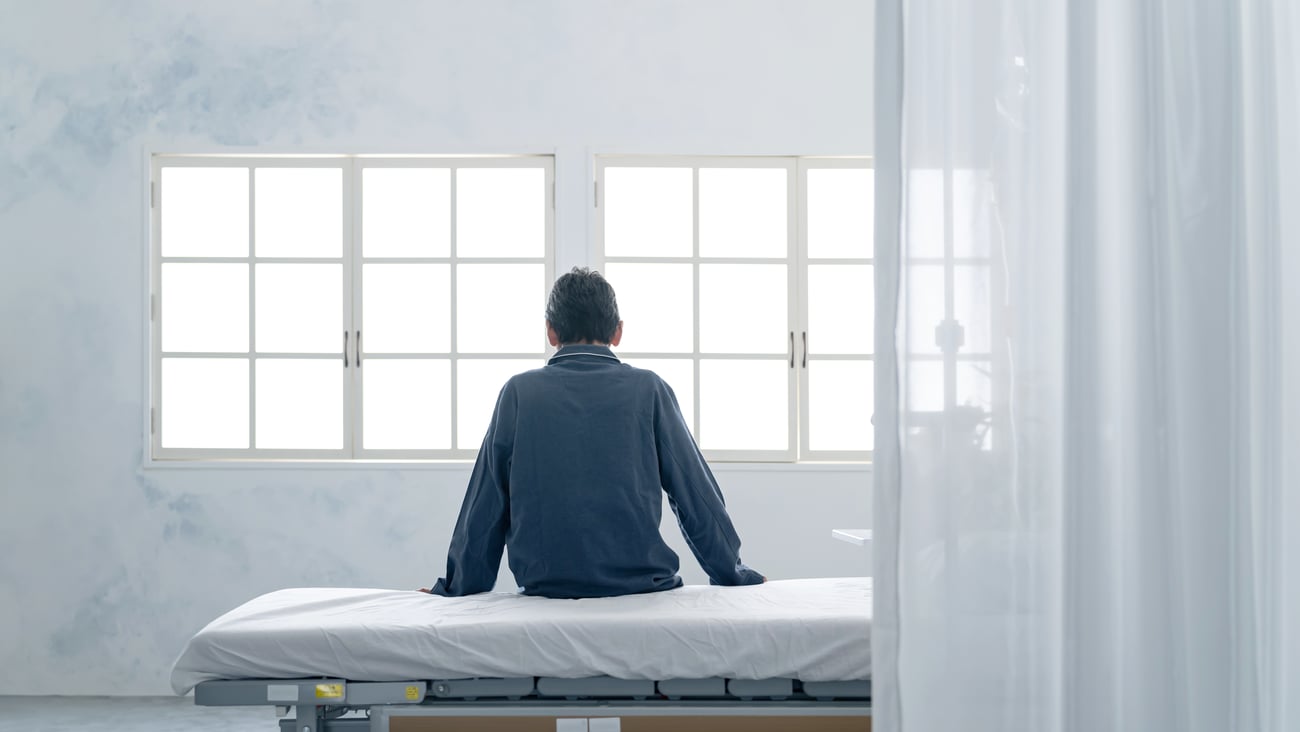 Depressed inpatient sitting on bed in hospital room