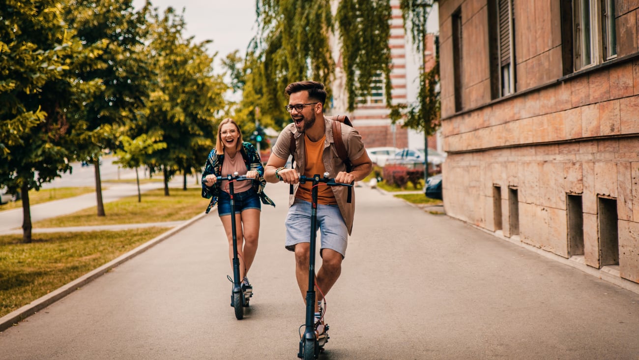 Young couple laughing as they ride e-scooters