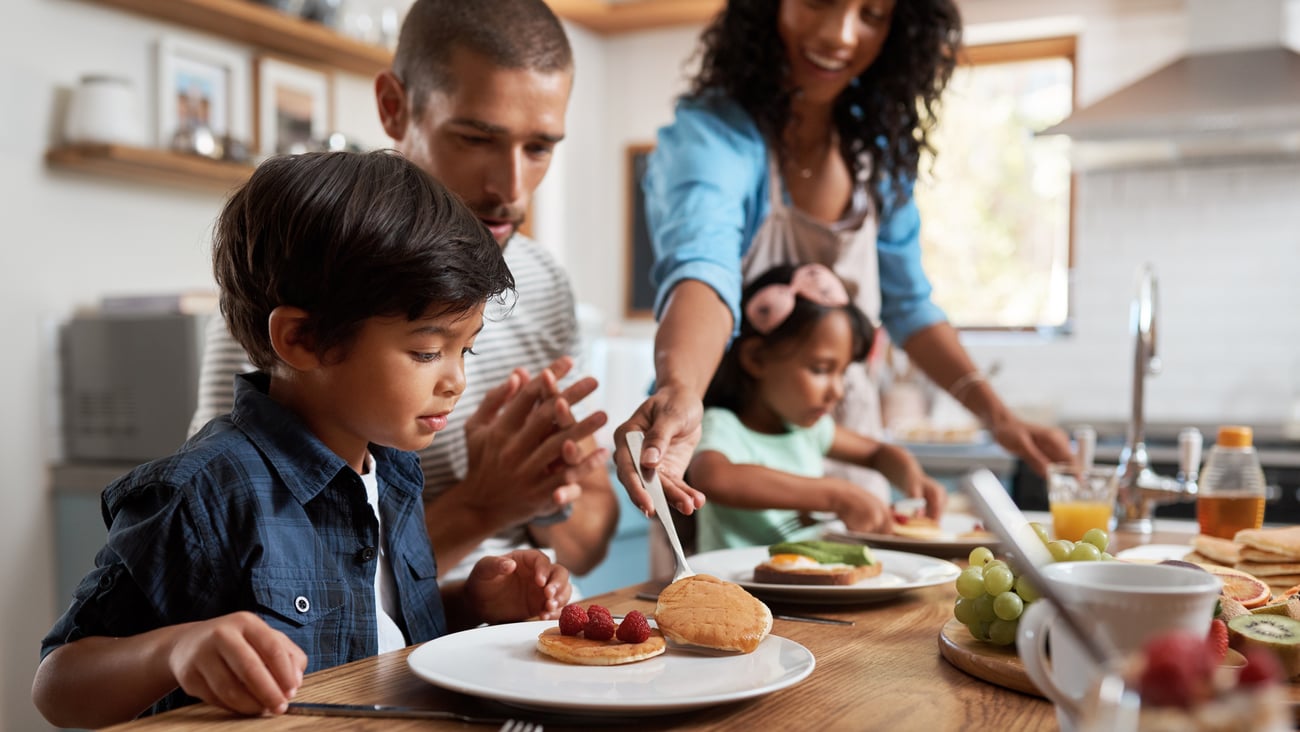Parents at kitchen table dishing up breakfast with two kids