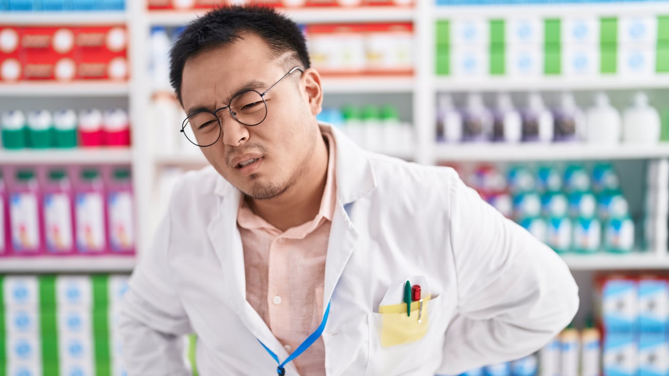 A chinese male pharmacist wincing and holding his painful back