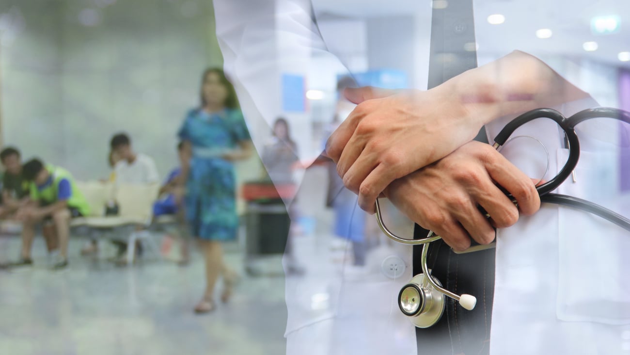 Close up of doctors folded hands holding a stethoscope with the blurry background of a hospital