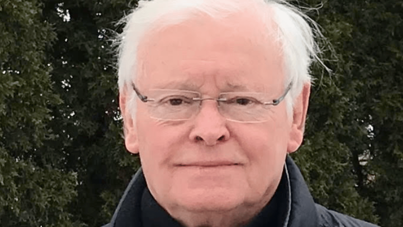 Older white man with glasses standing outside in a black jacket