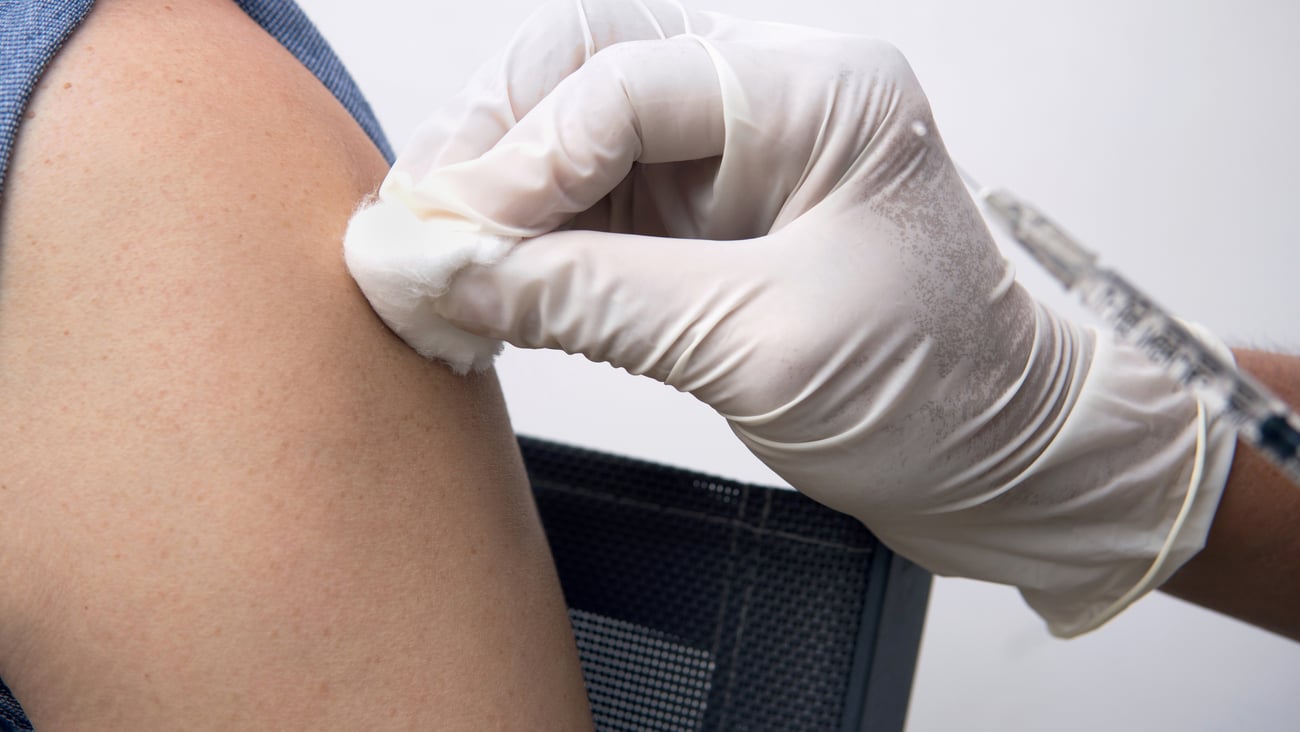 A healthcare provider swabs a shoulder before administering a vaccine. 