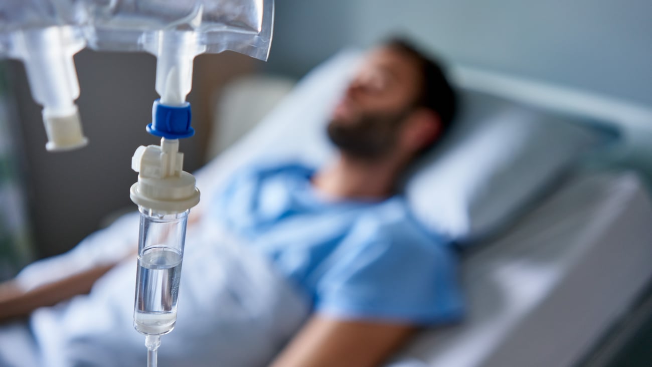 Intravenous drip treatment being used to treat a sick man lying on a bed in a hospital 