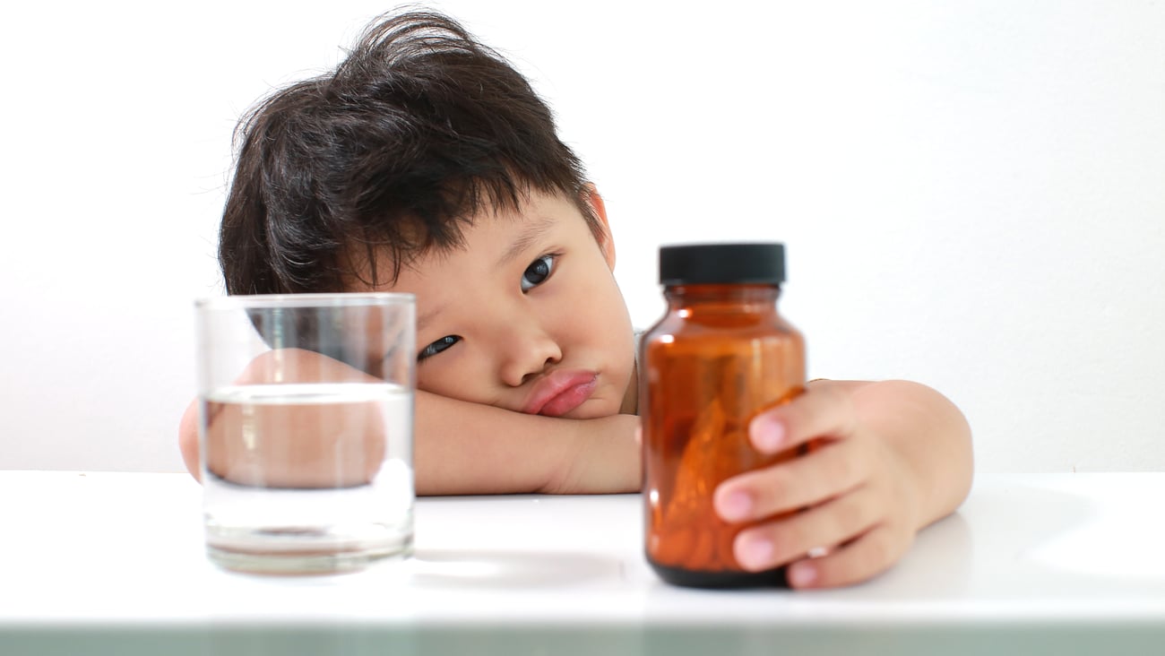 Young boy sadly contemplating a bottle of pills, uninterested in taking his medicine