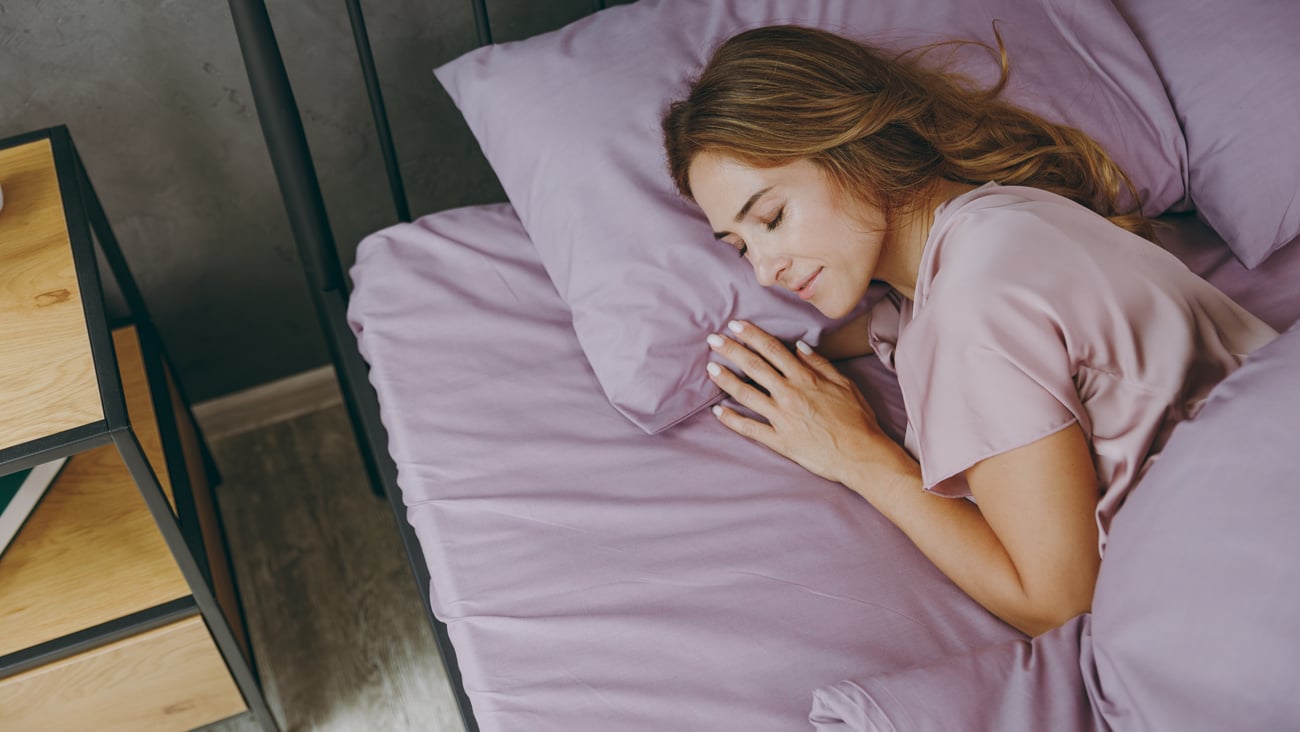 Middle aged woman sleeping in purple bedding