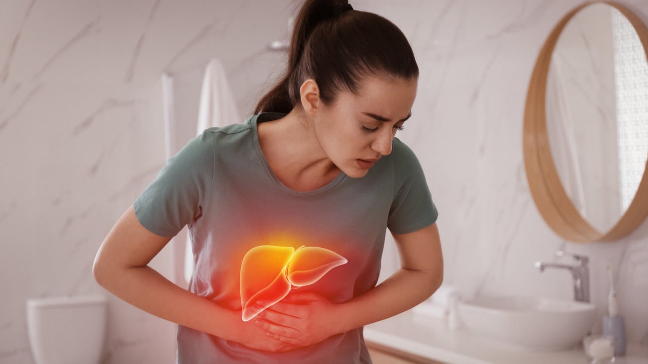 Young woman holding her abdomen with a cartoon red liver superimposed to highlight this is the organ giving her pain