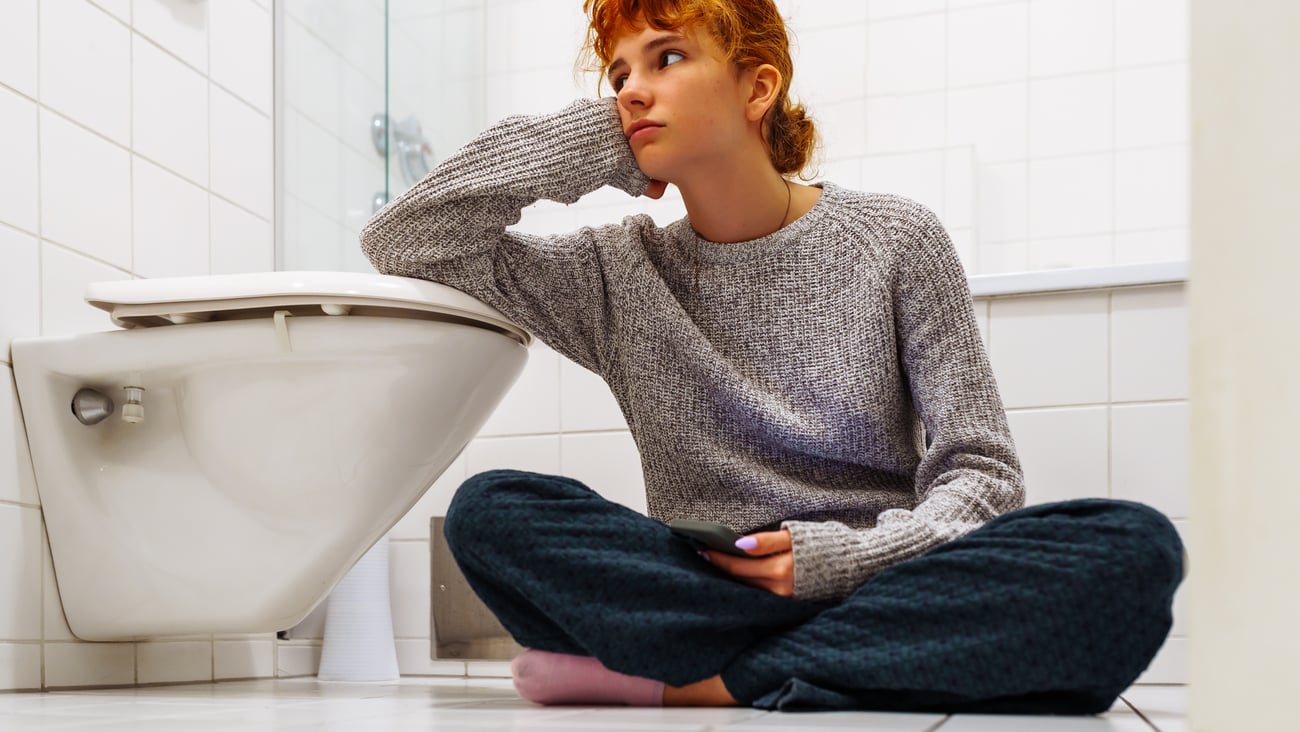 Young woman sitting beside a toilet on the floor looking despondent