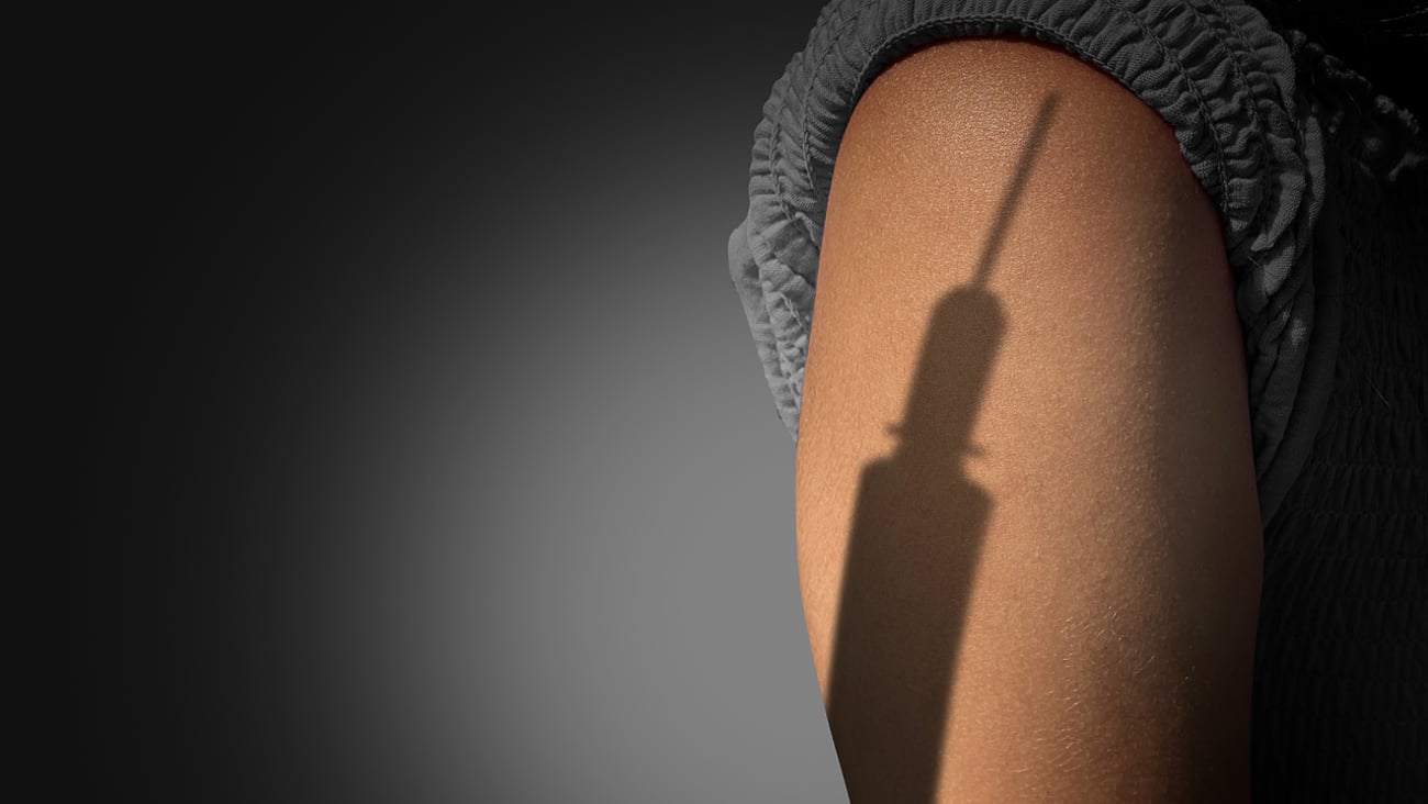 The shadow of a syringe looming over a woman's arm