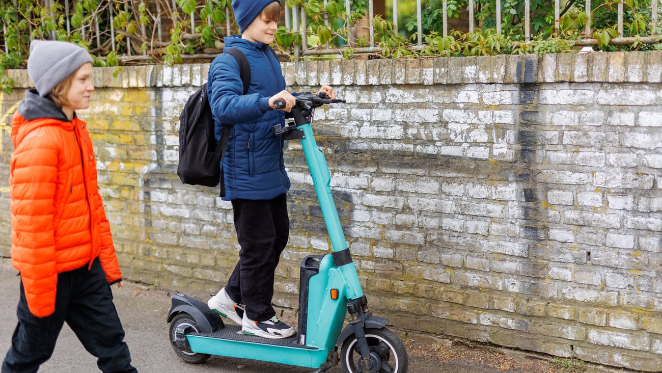 Two boys without helmets playing with an e-scooter