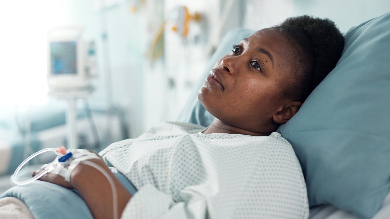 Young Black woman lying in bed in a hospital looking despondent 