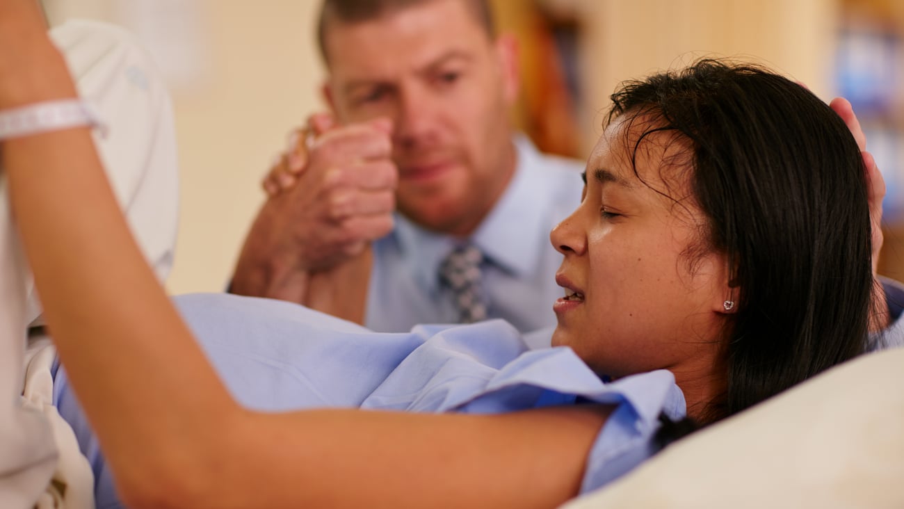 Young woman giving birth with her partner beside her holding her hand