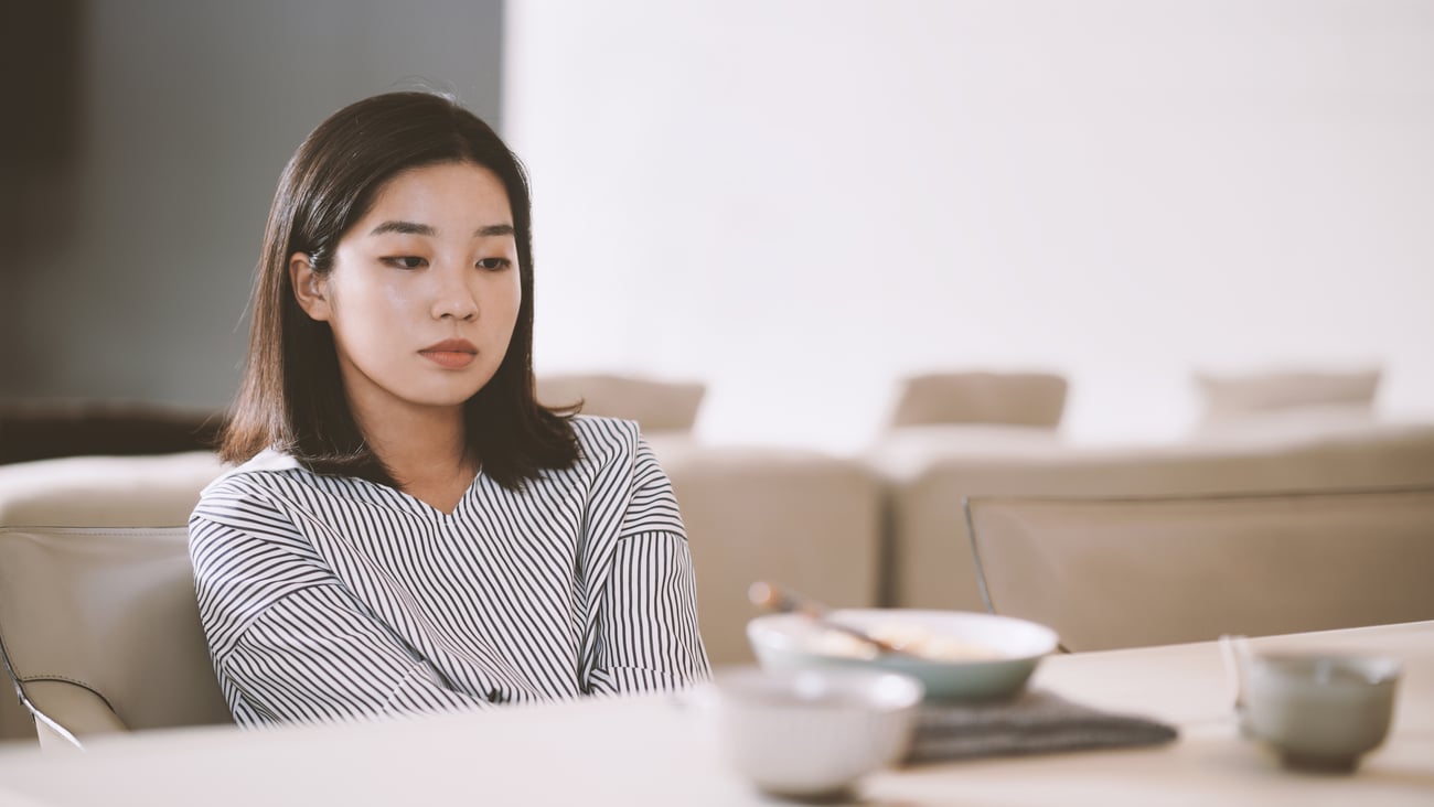 Young Asian woman sitting looking despondent with a plate of food in the foreground