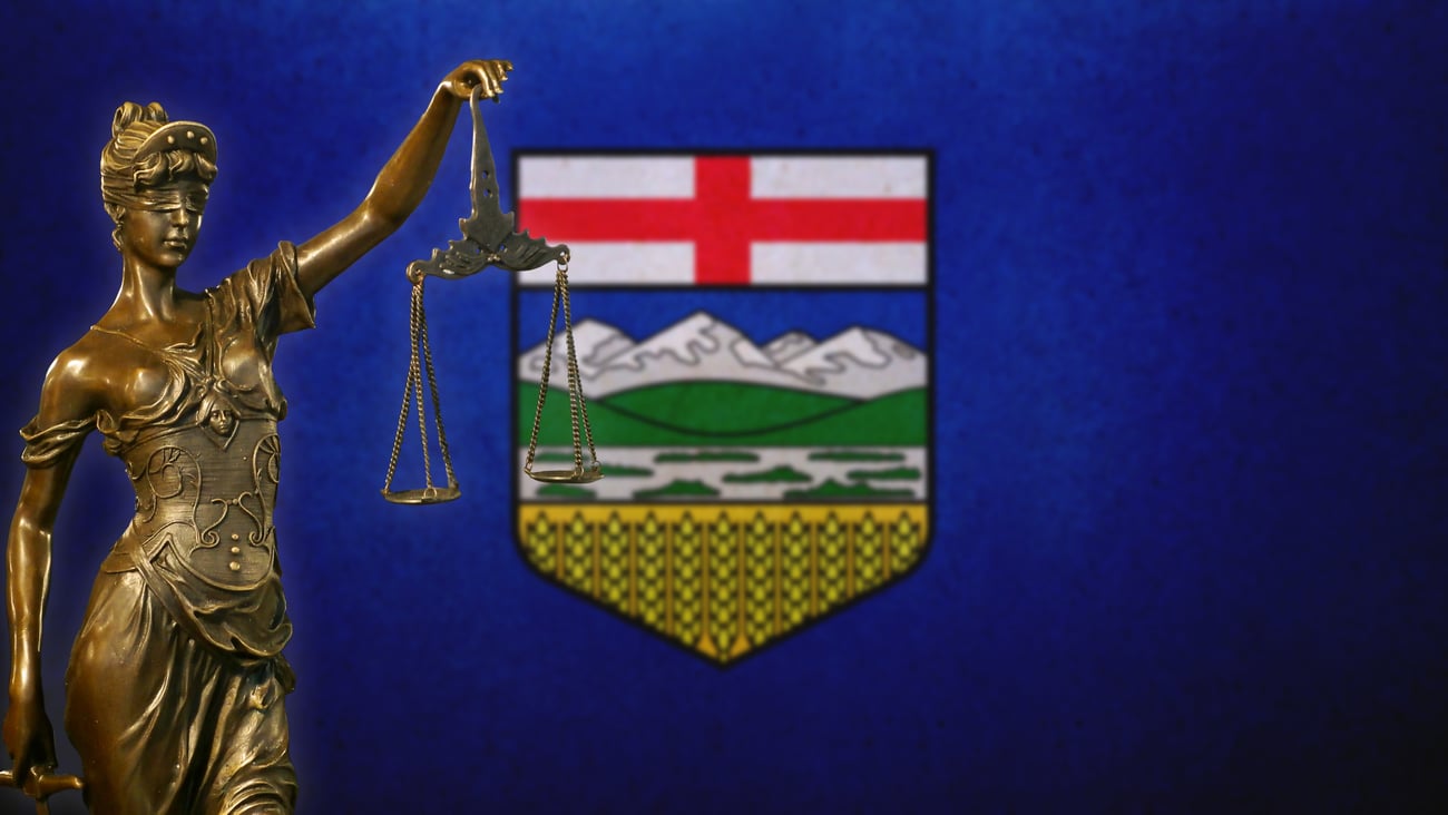A bronze statue of Justice holding scales with the Alberta flag in the background