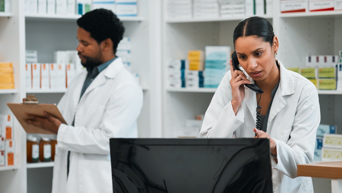 Black female pharmacist on cellphone and computer in dispensary